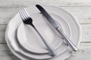 A minimalist setting of elegant white plates with cutlery on a rustic wooden table, perfect for dining themes.